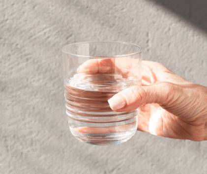 A hand holding a clear glass of water against a textured gray background.