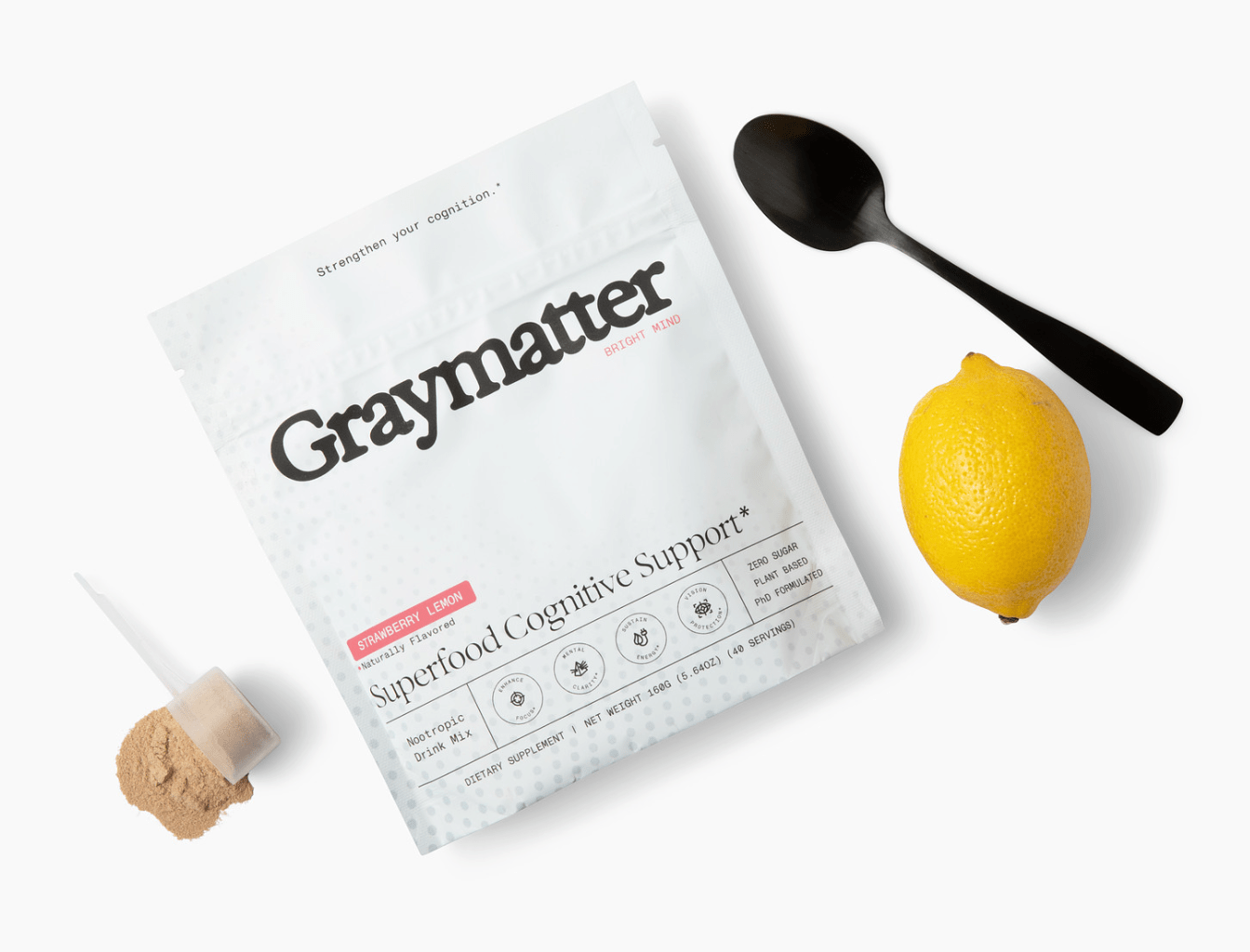 Graymatter cognitive support drink mix with a lemon, spoon, and scoop of powder.